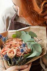 Image showing Young girl with red hair holds beautiful bunch of roses living coral colored. Close-up. Conept of celebrating of Mother\'s Day.