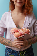 Image showing A bouquet of pink roses is holding in hands a sexy red-haired girl around a blue background with copy space. Valentine\'s day concept