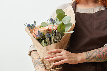 Image showing Fresh flowers living coral roses and eryngium as a congratulate bouquet in girl\'s hand with tattoo, copy space. Post card for Mother\'s Day.