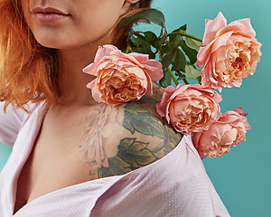 Image showing Young cute girl with tattoo on her shoulders and a bouquet of coral roses on a blue background. Postcard to Mother\'s day.