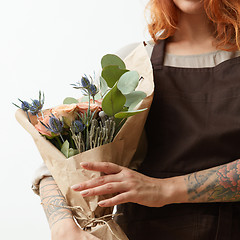 Image showing Young girl with ginger hair hold beautiful bunch with fresh natural flowers and leaves on a light background, copy space. Holiday card.