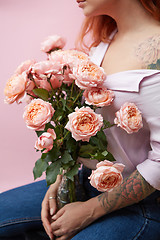 Image showing A glass vase with delicate pink roses holds a girl with a tattoo around a pink background with space for text. Mothers Day