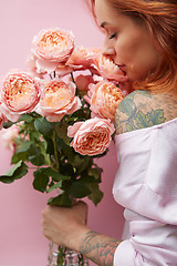 Image showing Pretty woman with ginger hair, tattoo on her shoulder and hands, holds bouquet of roses on a living coral background. Card on Woman\'s or Mother\'s Day.