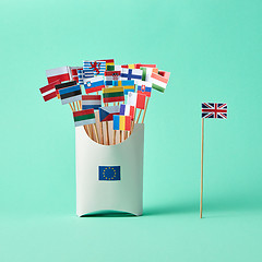 Image showing Different paper flags in a cardboard box with an EU sign and flag of Britain aside on green background with copy space. The exit of Britain from the EU