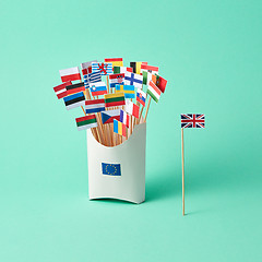 Image showing Paper flag of Britain and a cardboard box with a sign of the EU and different flags on a green background with copy space. The exit of Britain from EU