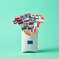 Image showing Set of different paper flags in cardboard box decorated with EU sign on green background with copy space. Economic, Political Union of European States