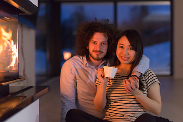 Image showing happy multiethnic couple sitting in front of fireplace