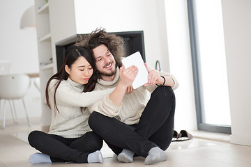 Image showing multiethnic couple using tablet computer in front of fireplace