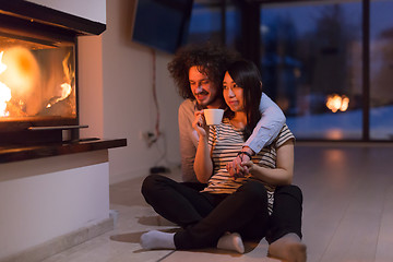 Image showing happy multiethnic couple sitting in front of fireplace