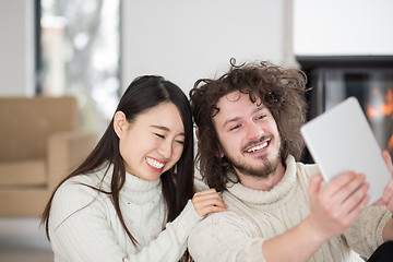 Image showing multiethnic couple using tablet computer in front of fireplace