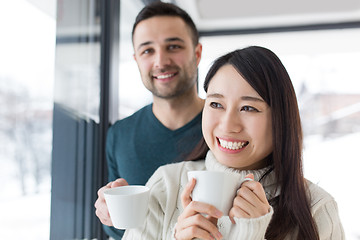 Image showing multiethnic couple enjoying morning coffee by the window