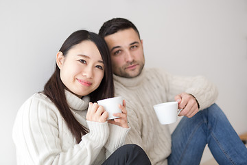 Image showing multiethnic couple enjoying morning coffee by the window