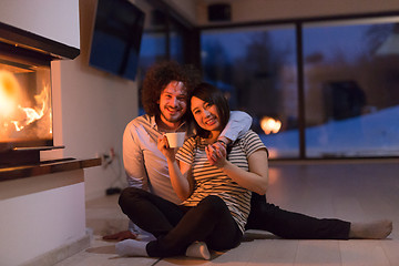 Image showing happy multiethnic couple sitting in front of fireplace