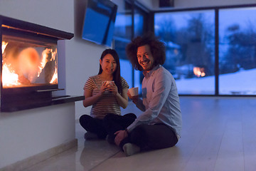 Image showing happy multiethnic couple sitting in front of fireplace