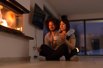 Image showing happy multiethnic couple sitting in front of fireplace