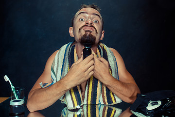 Image showing young man in bedroom sitting in front of the mirror scratching his beard