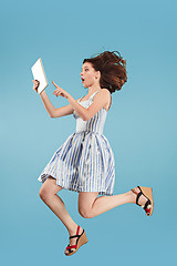 Image showing Image of young woman over blue background using laptop computer or tablet gadget while jumping.