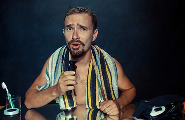 Image showing young man in bedroom sitting in front of the mirror scratching his beard