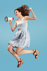 Image showing Beautiful young woman jumping with megaphone isolated over blue background