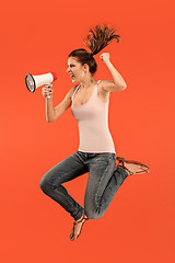 Image showing Beautiful young woman jumping with megaphone isolated over red background