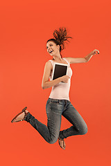 Image showing Image of young woman over blue background using laptop computer or tablet gadget while jumping.