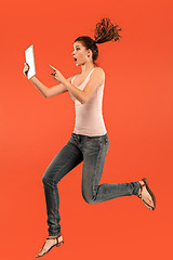 Image showing Image of young woman over blue background using laptop computer or tablet gadget while jumping.