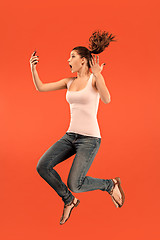 Image showing Image of young woman over blue background using laptop computer or tablet gadget while jumping.