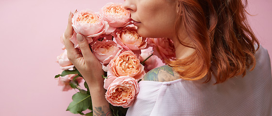 Image showing Red-haired woman with tattoo on her shoulders holds delicate fresh coral roses on a living coral background. A gift for Mother\'s Day. Copy space.