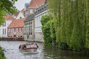 Image showing Bruges, Belgium - May 17, 2012: Old houses on the water channel, with trees and a floating motor boat on a spring day.