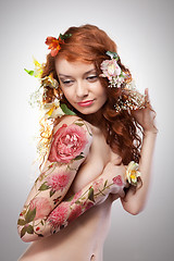 Image showing Beautiful red-haired girl with tattoo adorned with flowers on a gray background with copy space. Spring concept