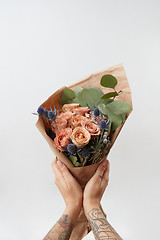 Image showing Woman\'s hands hold colourful blossoming flower bouquet of fresh roses living coral color on a gray background. Copy space. Mother\'s and Woman\'s Day.