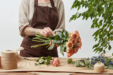Image showing Female florist making beautiful bouquet from living coral color roses on a light background. Process step by step