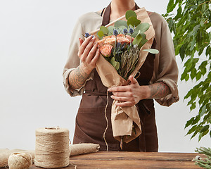 Image showing Woman florist with fresh beautiful handmade bouquet from fesh fragrant flowers ang green leaves on a light wall background, copy space.