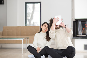 Image showing multiethnic couple using tablet computer in front of fireplace