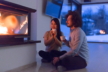 Image showing happy multiethnic couple sitting in front of fireplace