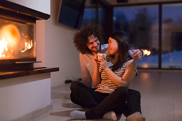 Image showing happy multiethnic couple sitting in front of fireplace