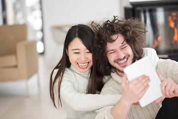 Image showing multiethnic couple using tablet computer in front of fireplace