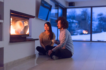 Image showing happy multiethnic couple sitting in front of fireplace