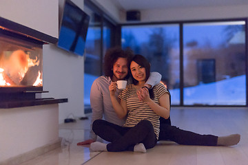 Image showing happy multiethnic couple sitting in front of fireplace