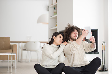 Image showing multiethnic couple using tablet computer in front of fireplace