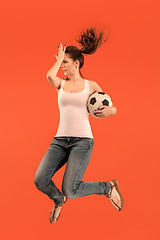 Image showing Forward to the victory.The young woman as soccer football player jumping and kicking the ball at studio on a red