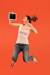 Image showing Image of young woman over blue background using laptop computer or tablet gadget while jumping.