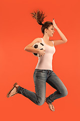 Image showing Forward to the victory.The young woman as soccer football player jumping and kicking the ball at studio on a red