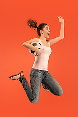 Image showing Forward to the victory.The young woman as soccer football player jumping and kicking the ball at studio on a red