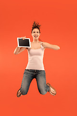 Image showing Image of young woman over blue background using laptop computer or tablet gadget while jumping.