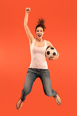 Image showing Forward to the victory.The young woman as soccer football player jumping and kicking the ball at studio on a red