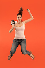 Image showing Beautiful young woman jumping with megaphone isolated over red background