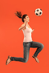 Image showing Forward to the victory.The young woman as soccer football player jumping and kicking the ball at studio on a red