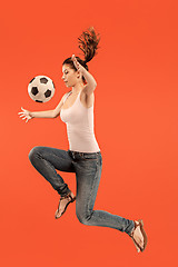 Image showing Forward to the victory.The young woman as soccer football player jumping and kicking the ball at studio on a red