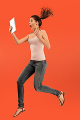 Image showing Image of young woman over blue background using laptop computer or tablet gadget while jumping.